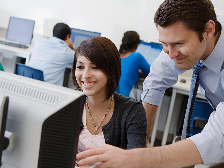 A teacher helps a student sitting at a computer